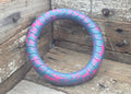 A tire-shaped dog toy with a blue and pink tread pattern, resting on rustic wooden boards.