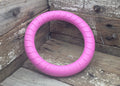 A pink textured circular dog tug toy labeled 'Fitness Rings' resting on rustic wooden boards.