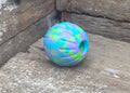 A colorful dog toy ball with a blue, green, and purple tie-dye pattern, resting on a weathered wooden surface.