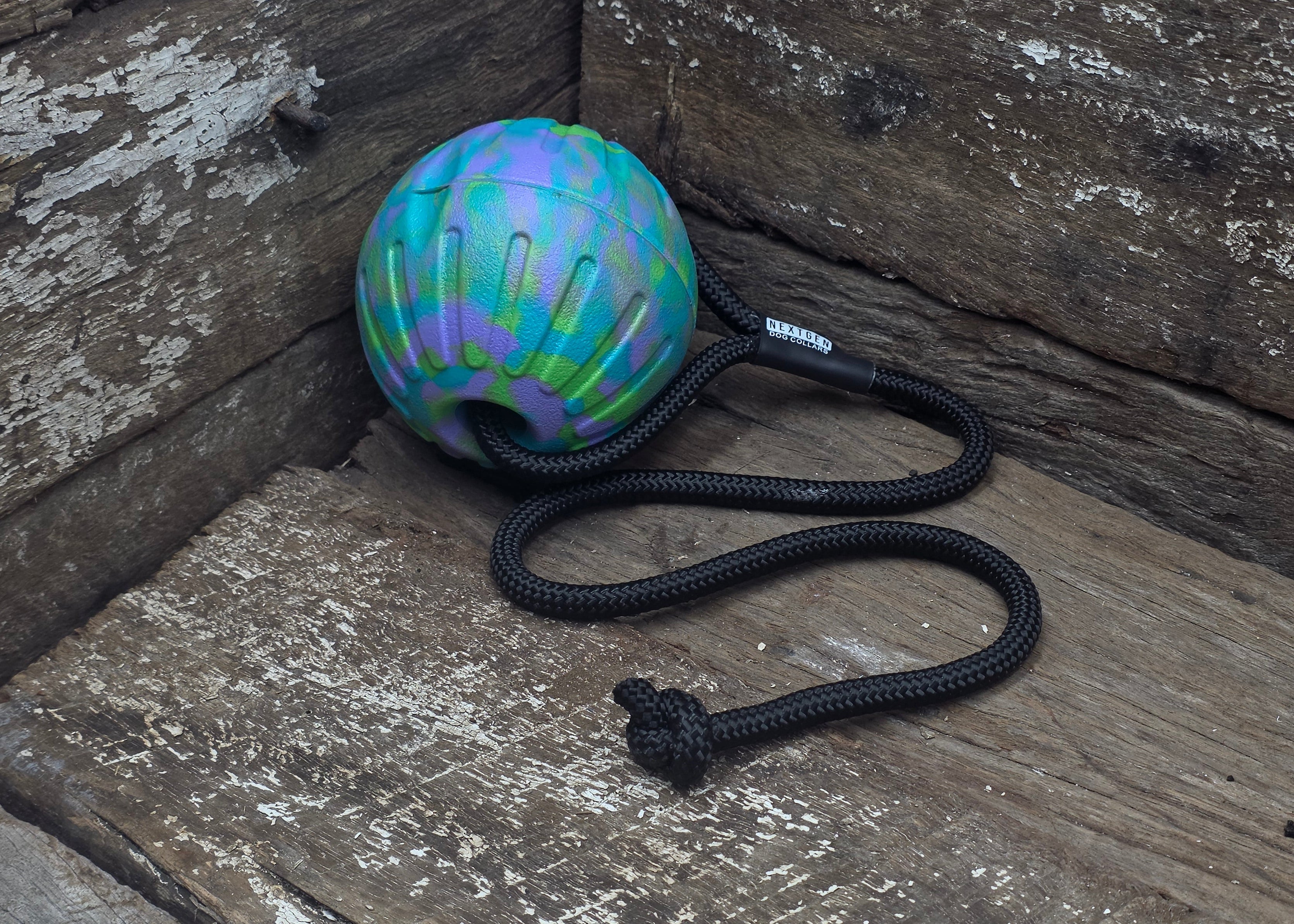 A colorful dog tug toy with a black rope, resting on a rustic wooden surface.