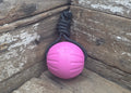 A pink textured ball toy attached to a black paracord leash, resting on rustic wooden boards.