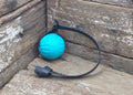 A turquoise ribbed ball with a black loop strap and black connector, resting on weathered wooden boards.