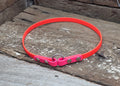A bright pink adjustable collar with silver metal rivets and a ring, resting on weathered wooden planks.