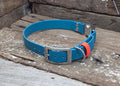 A bright blue leather dog collar with a silver metal buckle and a small orange accent tab, resting on weathered wooden boards.