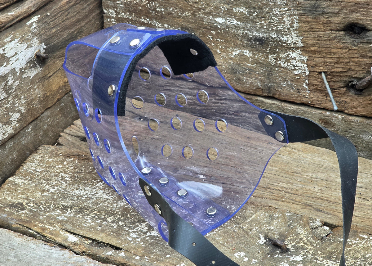 A clear plastic protective face mask with blue trim and black straps, resting on a rustic wooden surface.